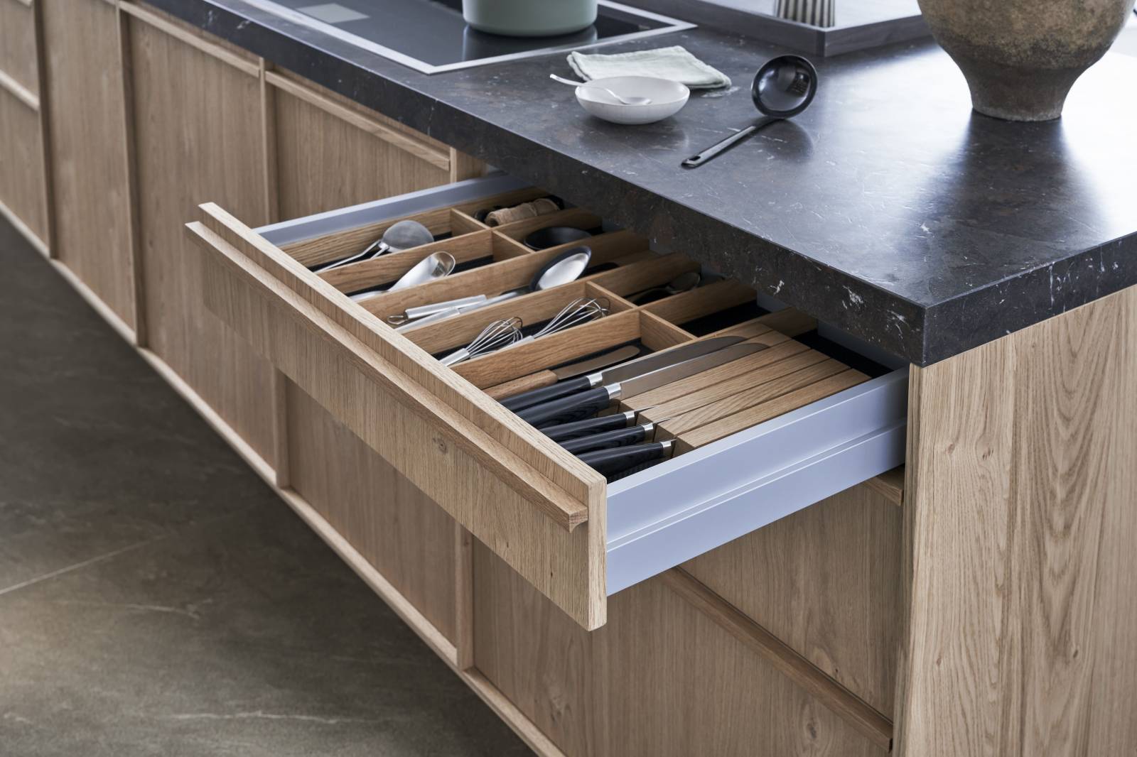 Cuisine haut de gamme en chêne clair, au design minimal et sans poignées, offrant des lignes épurées, des matériaux nobles et une ambiance moderne et élégante