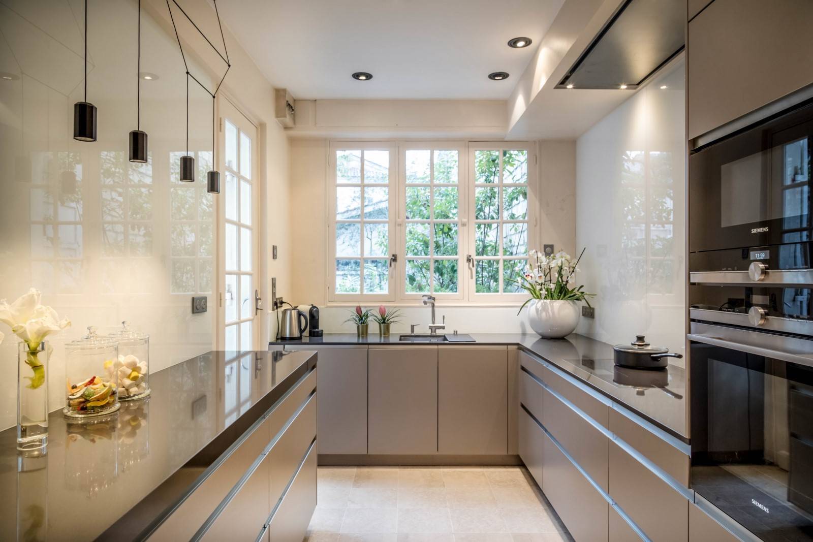 Cuisine moderne et épurée avec éclairage suspendu, matériaux haut de gamme, électroménagers intégrés et foyer design pour une ambiance chaleureuse